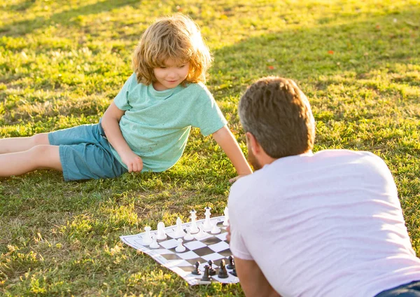 Táta a děcko hrají logickou hru. otec a syn hrají šachy na trávě. Den otců. šťastná rodina. — Stock fotografie