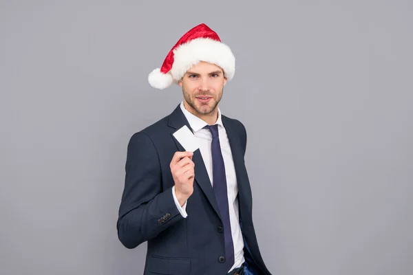 Biznesmen w czapce Mikołaja posiadają kartę kredytową z miejsca na kopiowanie na szarym tle, wyprzedaż świąteczna — Zdjęcie stockowe
