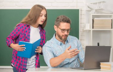 Meraklı çocuk ve baba sınıflarında ellerinde defter ve bilgisayarla oturuyorlar.