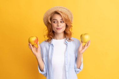 Gülümseyen, kıvırcık saçlı, yaz şapkalı, elmalı, vitaminli genç bir kadın.