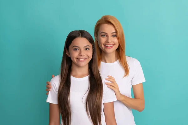 Liefdevolle moeder knuffel dochter in witte shirts op blauwe achtergrond, familie — Stockfoto