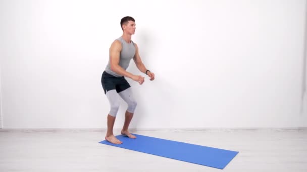 Атлет мускулистый парень делает приседания упражнения на фитнес коврик белый фон, держать себя в форме — стоковое видео