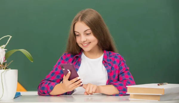 Happy child at school chatting on phone on blackboard background, communication — Stock Photo, Image