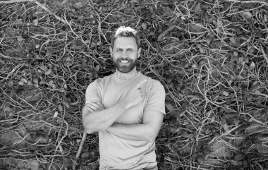 Yazlık gömlekli mutlu sakallı, olgun bir adam doğal arka planı işaret ediyor.