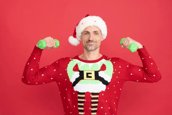 Feliz hombre de Santa Claus brazos flexibles con pesas de mano haciendo ejercicios de mancuerna fondo rojo, Navidad —  Fotos de Stock