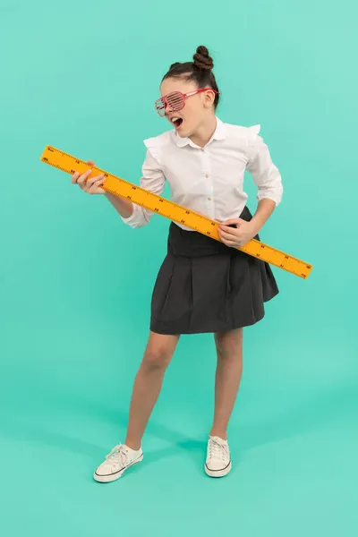 Радостная девушка носить униформу и очки проведения математики линейку на синем фоне, измерения — стоковое фото
