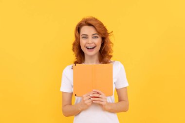 Mutlu bir kadın sarı arka plan ve bilgi üzerine kitap tutar.