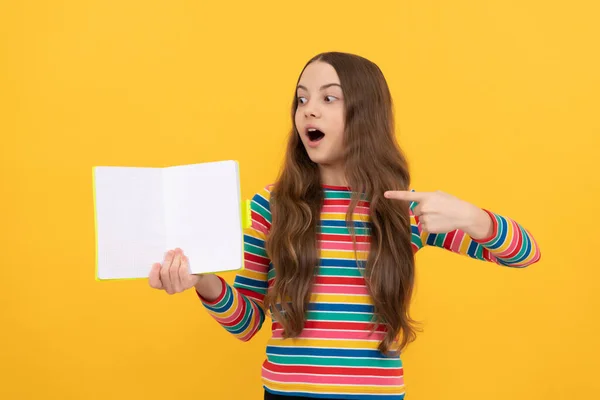 Surprised girl child point finger at open book for copy space yellow background, pointing — Stock Photo, Image