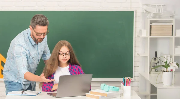 Zvědavý kluk a táta sedí ve třídě s počítačem na tabuli, zpátky do školy — Stock fotografie