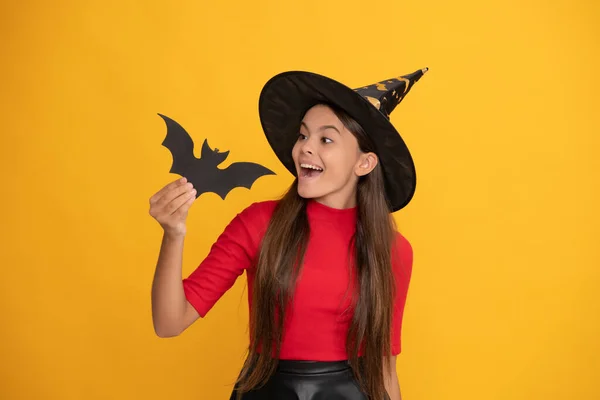 Positivo adolescente chica usando bruja sombrero celebración de murciélago en amarillo fondo, infancia — Foto de Stock