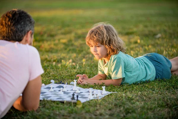 Šťastná rodina rodiče a dítěte hraje šachy na zelené trávě v parku venkovní, rodinné vztahy. — Stock fotografie