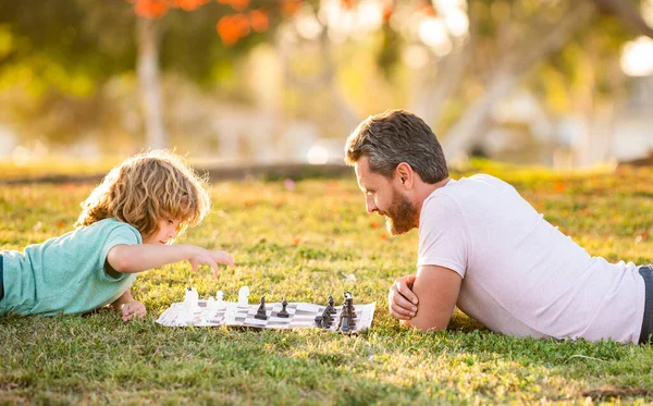 Família feliz de pai e filho criança jogando xadrez na grama verde no parque ao ar livre, dia dos pais — Fotografia de Stock