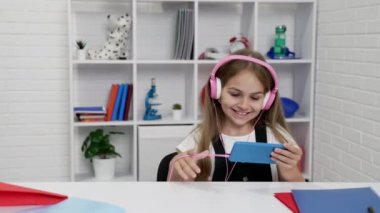 Modern kulaklıklı mutlu çocuk sınıfta akıllı telefondan video izliyor, modern eğitim...