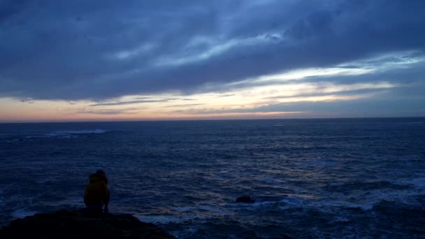 Медленные движения женщины в пиджаке сидя глядя на волнистое море с драматическим небом, ожидая вдохновения — стоковое видео