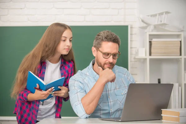 Enfant attentif et papa assis dans la salle de classe avec copybook et ordinateur au tableau noir, travaux scolaires — Photo