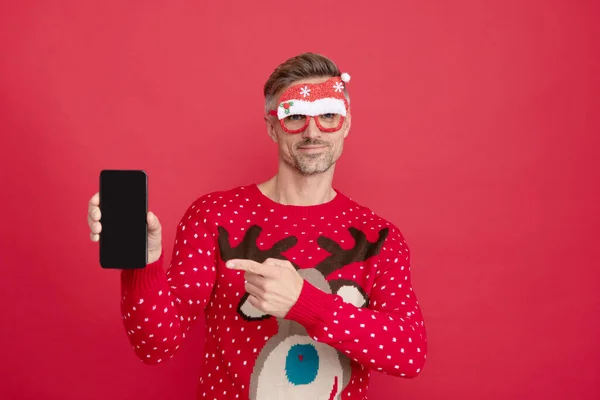 Facet od świąt wskazuje palcem na ekranie telefonu na czerwonym tle. Szczęśliwego Nowego Roku. — Zdjęcie stockowe