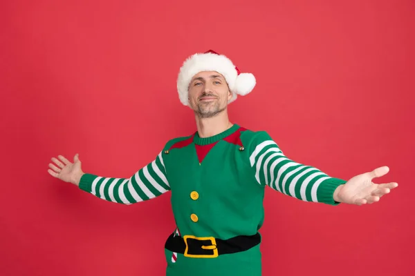 Um homem feliz disfarçado de duende. Xmas cara em chapéu de Papai Noel em fundo vermelho. feliz ano novo. — Fotografia de Stock