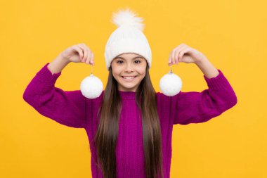 Kış şapkalı mutlu çocuk. Süslü topları olan çocuk. Genç kız sarı arka planda kartopu tutuyor..