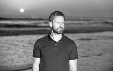 Yazlık gömlekli sakallı yakışıklı adam sahilde gün batımını seyrediyor, rahatla.