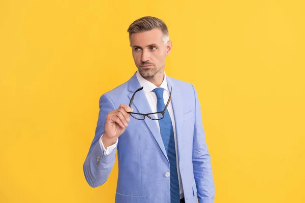 Hombre de negocios maduro en elegante chaqueta mantenga las gafas sobre fondo amarillo, visión — Foto de Stock