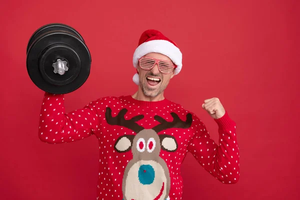 Hombre alegre en suéter de invierno y sombrero de Santa Claus. chico de Navidad mantenga las barras sobre fondo rojo. —  Fotos de Stock