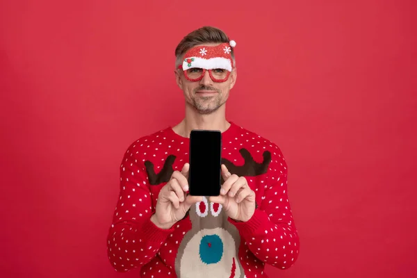 Prezentace. Veselý muž ve svetru a brýlích. xmas chlap prezentující obrazovku telefonu — Stock fotografie