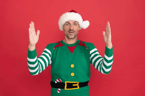 Homem espantado com traje de duende. Xmas cara em chapéu de Papai Noel em fundo vermelho. feliz ano novo. — Fotografia de Stock