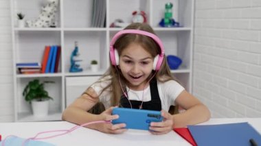 Kulaklıklı mutlu çocuk sınıfta telefonla video seyrediyor.