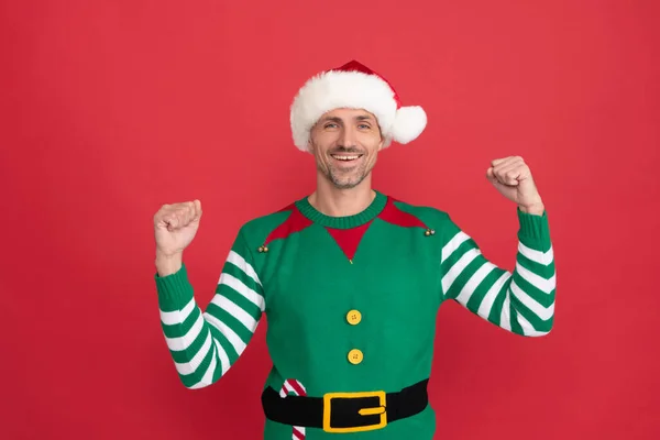 Feliz hombre exitoso en traje de elfo. chico de Navidad en Santa Claus sombrero sobre fondo rojo. —  Fotos de Stock