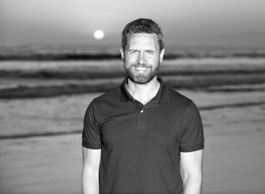 Gün batımında deniz üzerinde sakallı neşeli bir adam. Sahilde tıraş olmamış mutlu bir adam..