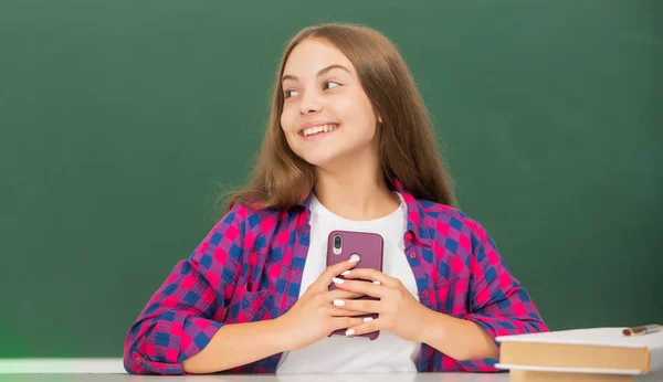 Glückliches Kind in der Schule plaudert am Telefon auf Tafel Hintergrund, Nachricht — Stockfoto