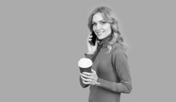 Щаслива дівчина розмовляє на мобільному телефоні, тримаючи гарячу чашку чаю або кави, п'є сірий фон, перерва — стокове фото