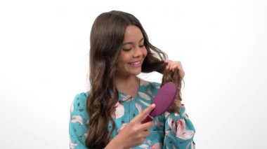 Neşeli genç kız uzun, sağlıklı, dalgalı saçlarını tarıyor saç fırçasıyla güçlerini ve saç bakımlarını gösteriyor.