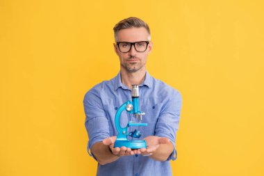 Sarı arka planda mikroskop gösteren gözlüklü olgun bir adam, veri bilimi