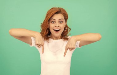 Şaşkın kızıl saçlı kadın mavi arka planı işaret ediyor, fotokopi alanı, alışveriş satışları....