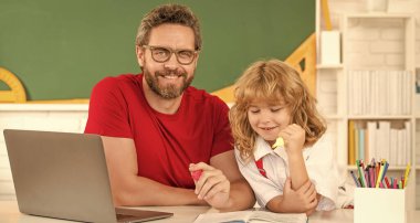 Baba-oğul sınıfta dizüstü bilgisayarla, online eğitimle okuyor.