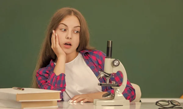 Erstaunt Teenie-Mädchen mit Mikroskop in der High School an der Tafel, Biologie — Stockfoto