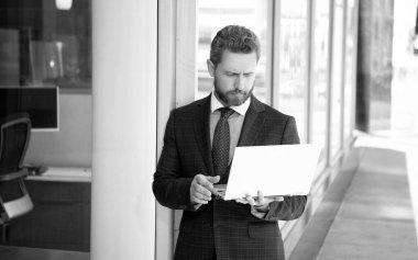 Ciddi sakallı, yetişkin, takım elbiseli serbest çalışan iş yerinde dizüstü bilgisayarla sohbet eden, internette sohbet eden...