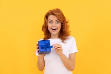 amazed woman with present box on yellow background, boxing day