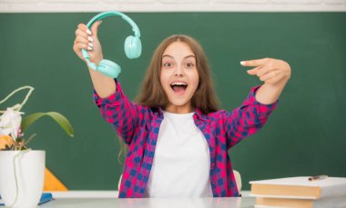 Şaşkın çocuk kulaklığı karatahtaya, çocukluğa doğrultuyor.