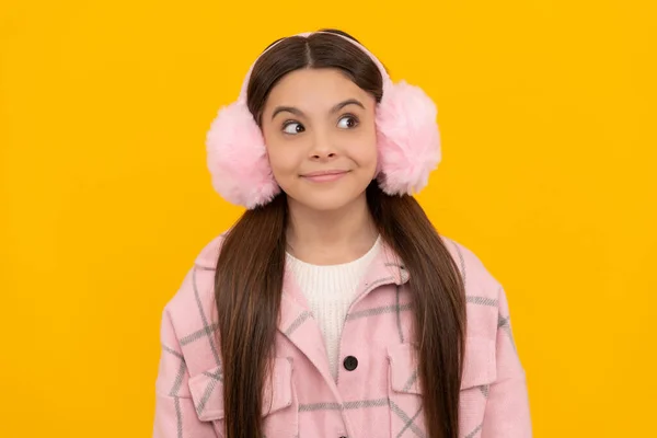 Happy girl child in warm winter fur earmuffs smile with sly look yellow background, intrigue — 스톡 사진