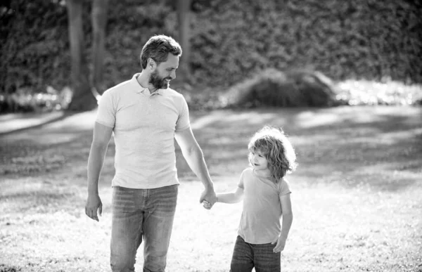 Happy son and father holding hands walking on sunny summer day in park grass, fatherhood — Stock Photo, Image