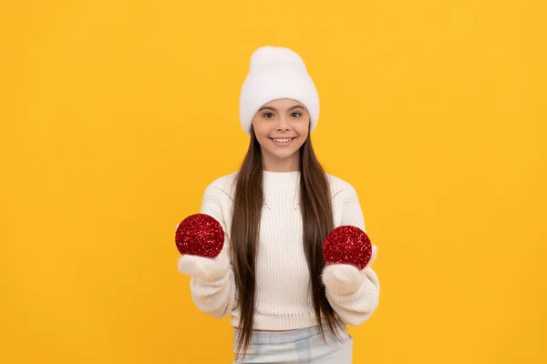 Happy kid in winter hat and gloves hold decorative new year balls on yellow background, xmas — Fotografia de Stock