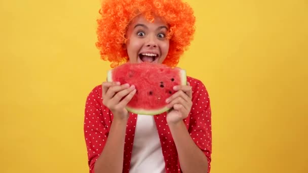 Happy kid in orange hair wig eating slice of water-melon fruit on yellow background, watermelon — Αρχείο Βίντεο
