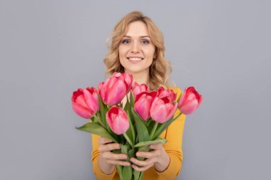 cheerful lady hold flowers for spring holiday on grey background. selective focus