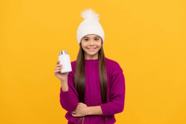 smiling child in winter hat with pill jar. food supplement. teen girl with natural pill products.