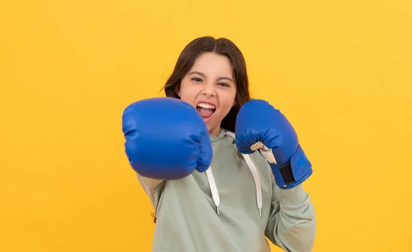 Aggressive child punching in boxing gloves on yellow background, sport — Stockfoto
