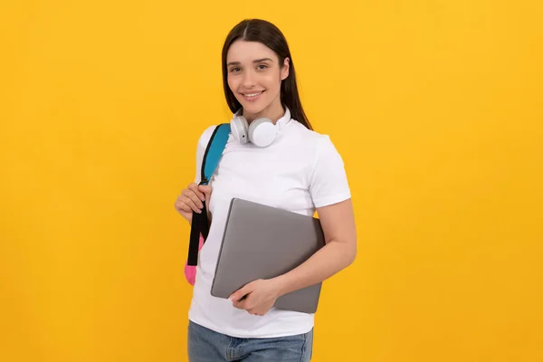 Happy woman with earphones and computer on yellow background, school — Stok fotoğraf