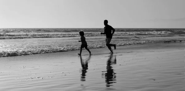 父亲和儿子的轮廓在夏天的海滩上奔跑，享受着自由，童年时代 — 图库照片