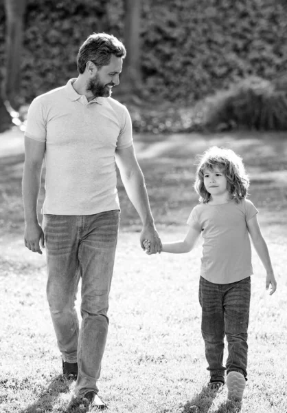 Feliz hijo y padre tomados de la mano caminando en el soleado día de verano en la hierba del parque, juntos — Foto de Stock